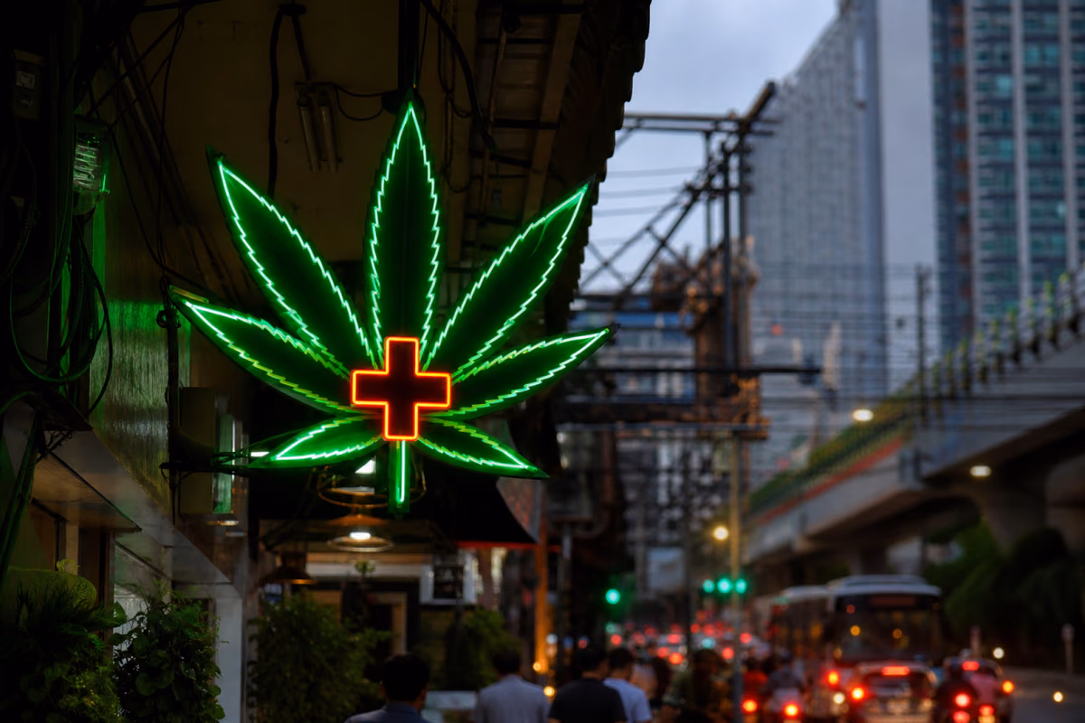 Letreiro de néon com folha de canábis e cruz médica sobre uma rua movimentada de Banguecoque